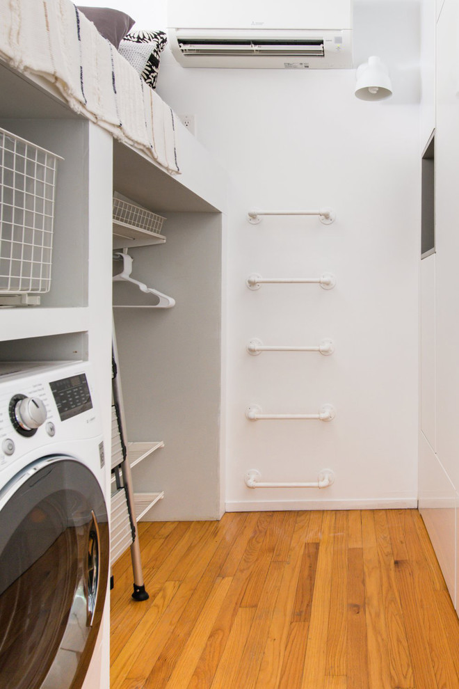Inspiration for a small modern single-wall laundry cupboard in Chicago with flat-panel cabinets, white cabinets, white walls, light hardwood floors, an integrated washer and dryer, brown floor and white benchtop.