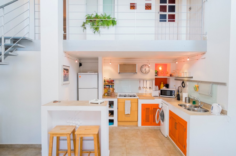 This is an example of a small mediterranean l-shaped eat-in kitchen in Malaga with a double-bowl sink, orange cabinets, white splashback, glass sheet splashback, white appliances, a peninsula, concrete benchtops and travertine floors.
