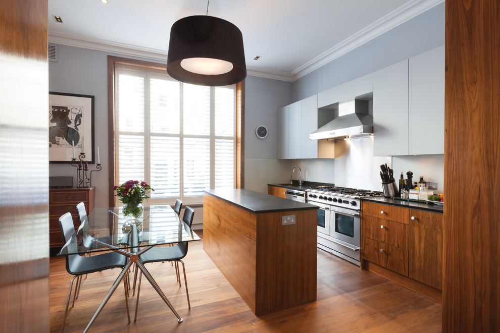 Inspiration for a mid-sized contemporary galley eat-in kitchen in London with flat-panel cabinets, medium wood cabinets, stainless steel appliances, medium hardwood floors, with island, a drop-in sink, granite benchtops, blue splashback, glass sheet splashback, brown floor and black benchtop.