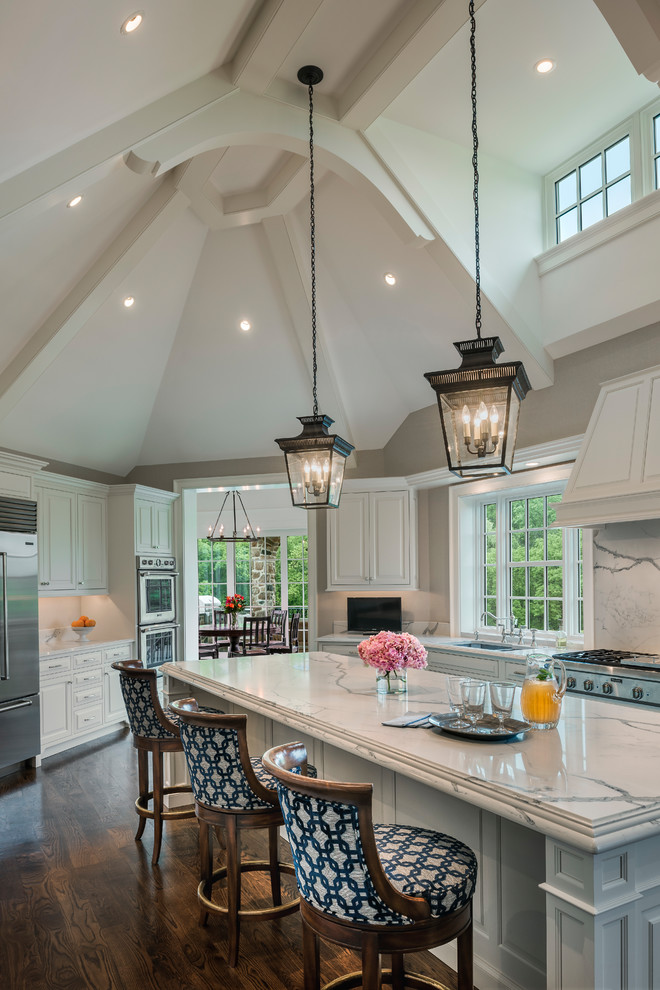Inspiration for a traditional u-shaped open plan kitchen in Philadelphia with an undermount sink, raised-panel cabinets, white cabinets, marble benchtops, stainless steel appliances, dark hardwood floors, with island, brown floor and white benchtop.