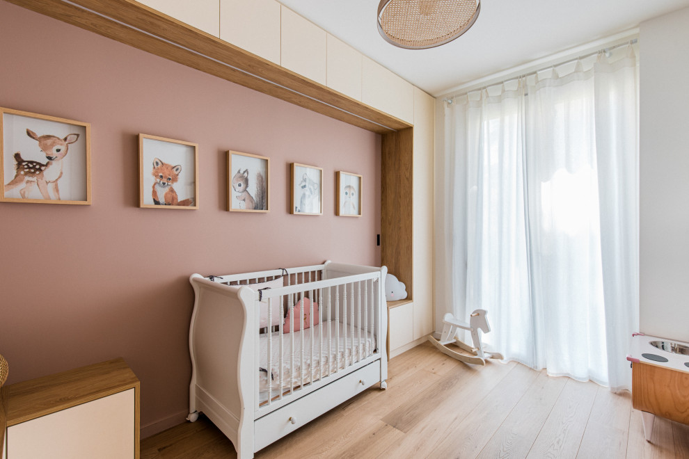 Medium sized scandi nursery for girls in Paris with pink walls, light hardwood flooring, all types of wall treatment and a feature wall.