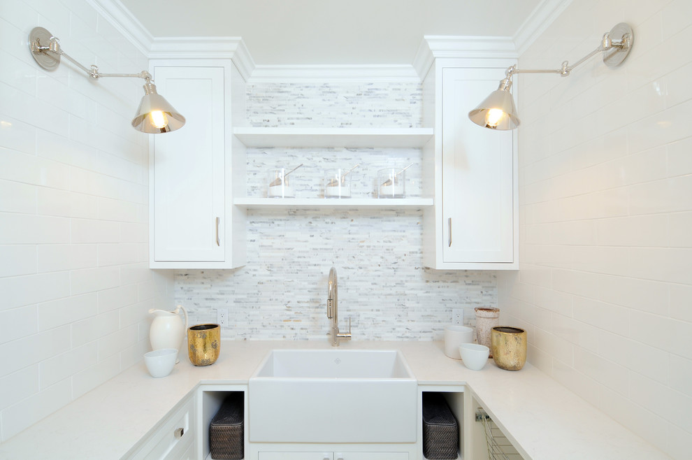 This is an example of a mid-sized transitional u-shaped dedicated laundry room in Los Angeles with a farmhouse sink, shaker cabinets, white cabinets, solid surface benchtops, white walls, painted wood floors and a side-by-side washer and dryer.