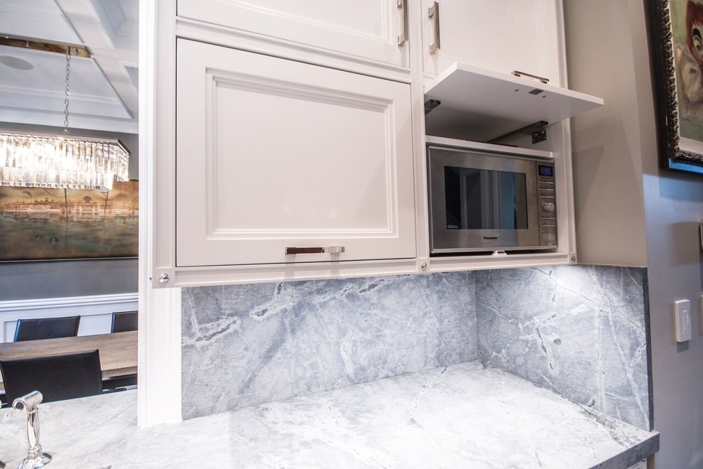 Mid-sized transitional u-shaped dark wood floor eat-in kitchen photo in Chicago with a farmhouse sink, recessed-panel cabinets, white cabinets, quartzite countertops, stone slab backsplash, stainless steel appliances, a peninsula and gray backsplash