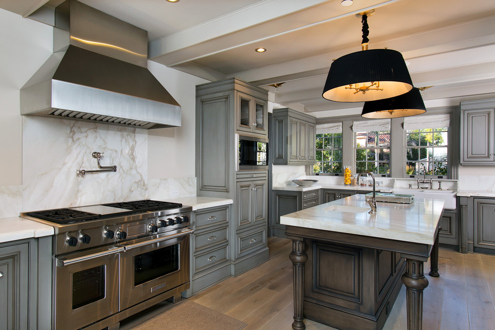 This is an example of an expansive traditional l-shaped eat-in kitchen in San Diego with a farmhouse sink, raised-panel cabinets, grey cabinets, grey splashback, stone slab splashback, stainless steel appliances and medium hardwood floors.