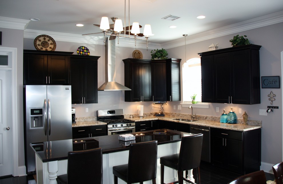 Mid-sized transitional l-shaped eat-in kitchen in Miami with an undermount sink, shaker cabinets, black cabinets, granite benchtops, beige splashback, stone slab splashback, stainless steel appliances, dark hardwood floors, with island and black floor.