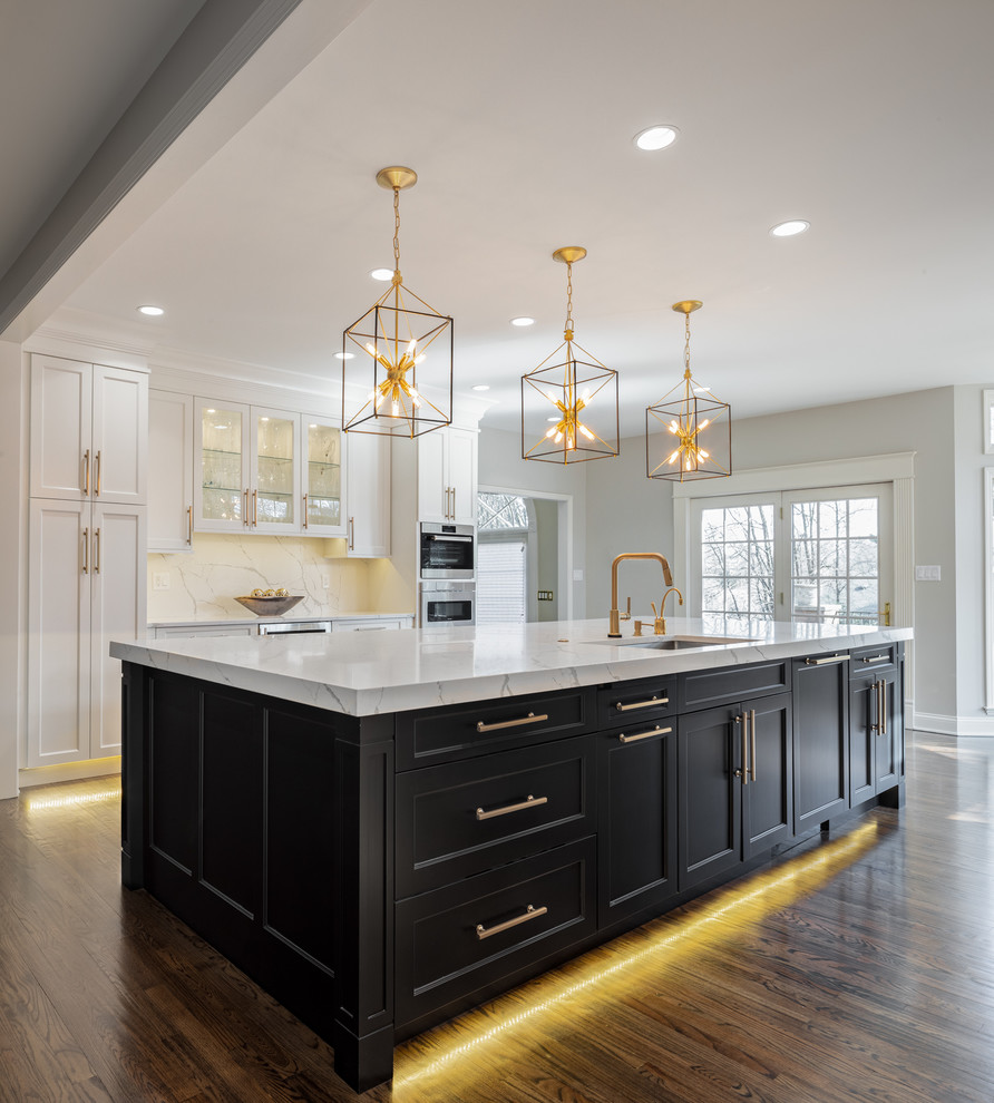 Large transitional u-shaped dark wood floor and brown floor kitchen photo in Other with an undermount sink, white cabinets, quartz countertops, white backsplash, stone slab backsplash, stainless steel appliances, an island, white countertops and shaker cabinets