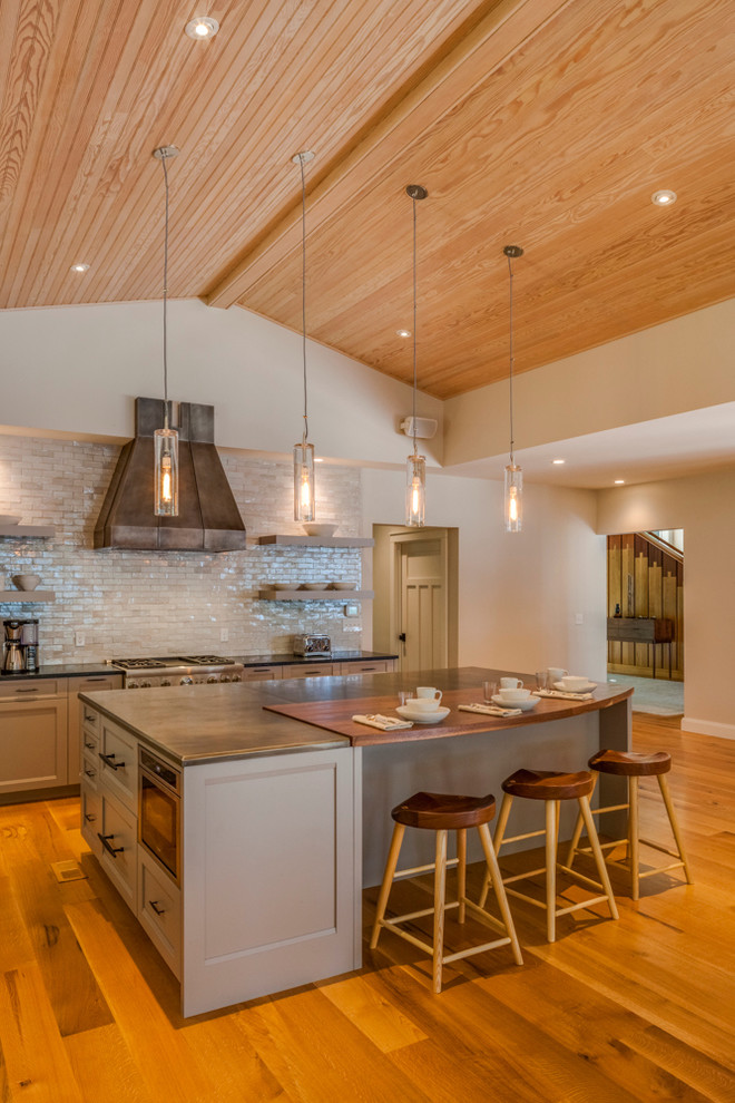 Expansive modern l-shaped open plan kitchen in Portland Maine with recessed-panel cabinets, grey cabinets, zinc benchtops, grey splashback, subway tile splashback, stainless steel appliances, medium hardwood floors and with island.