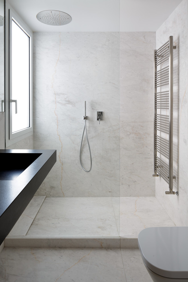 Modern master bathroom in Alicante-Costa Blanca with flat-panel cabinets, light wood cabinets, an open shower, a wall-mount toilet, marble, white walls, marble floors, an integrated sink, granite benchtops, white floor, an open shower and black benchtops.