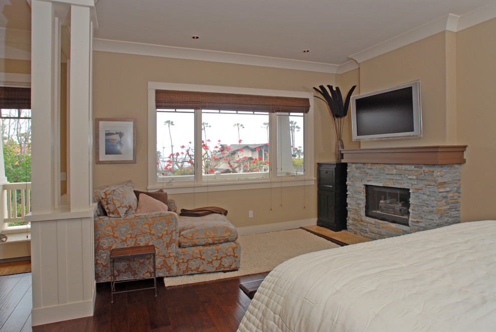 Inspiration for a large arts and crafts master bedroom in San Diego with beige walls, dark hardwood floors, a standard fireplace, a stone fireplace surround and brown floor.