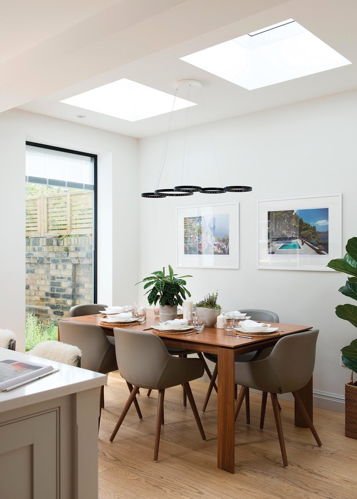 This is an example of a mid-sized contemporary kitchen/dining combo in London with white walls, light hardwood floors, beige floor and no fireplace.