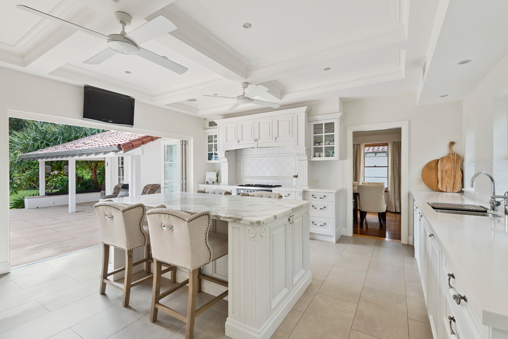 This is an example of a large traditional kitchen in Sydney with an undermount sink, beaded inset cabinets, white cabinets, marble benchtops, white splashback, ceramic splashback, stainless steel appliances, ceramic floors, with island, beige floor and white benchtop.