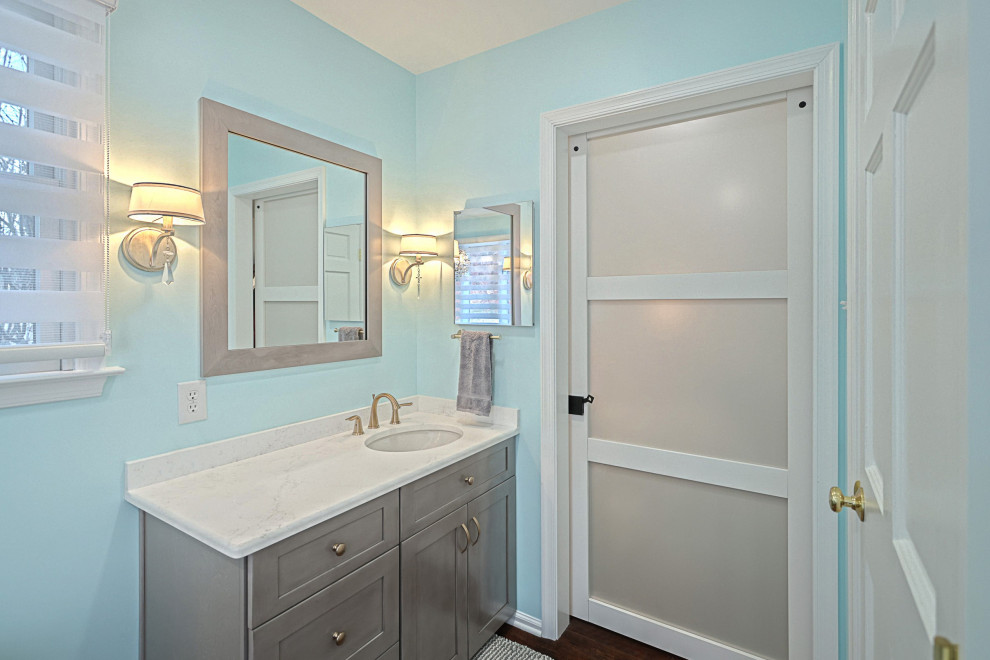 This is an example of a mid-sized transitional master wet room bathroom in Other with shaker cabinets, grey cabinets, a freestanding tub, a one-piece toilet, white tile, porcelain tile, blue walls, vinyl floors, an undermount sink, engineered quartz benchtops, brown floor, an open shower, white benchtops, a double vanity and a freestanding vanity.