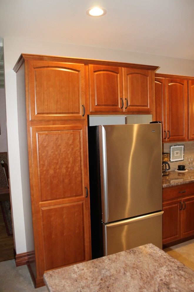 Example of a mid-sized mountain style l-shaped vinyl floor and beige floor eat-in kitchen design with a farmhouse sink, raised-panel cabinets, medium tone wood cabinets, laminate countertops, beige backsplash, cement tile backsplash, stainless steel appliances, a peninsula and beige countertops