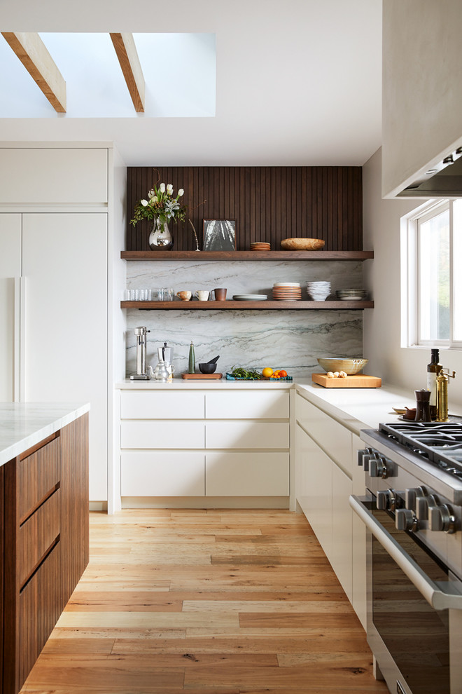 Inspiration for a scandinavian l-shaped eat-in kitchen in San Francisco with a single-bowl sink, flat-panel cabinets, white cabinets, green splashback, stone slab splashback, light hardwood floors, with island, white benchtop and stainless steel appliances.