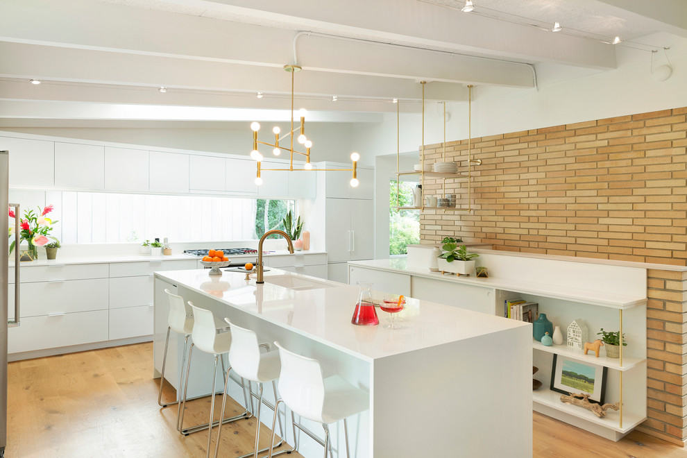 Inspiration for a midcentury u-shaped kitchen in Minneapolis with an undermount sink, flat-panel cabinets, white cabinets, window splashback, white appliances, light hardwood floors, with island and white benchtop.
