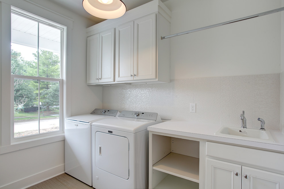 Design ideas for a small country single-wall dedicated laundry room in Grand Rapids with a drop-in sink, recessed-panel cabinets, laminate benchtops, white walls, laminate floors, a side-by-side washer and dryer and brown floor.