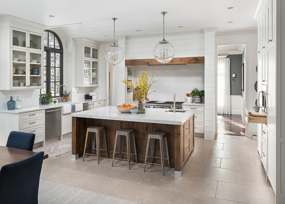 This is an example of a large transitional u-shaped eat-in kitchen in Chicago with a farmhouse sink, shaker cabinets, white cabinets, white splashback, stainless steel appliances, with island and beige floor.