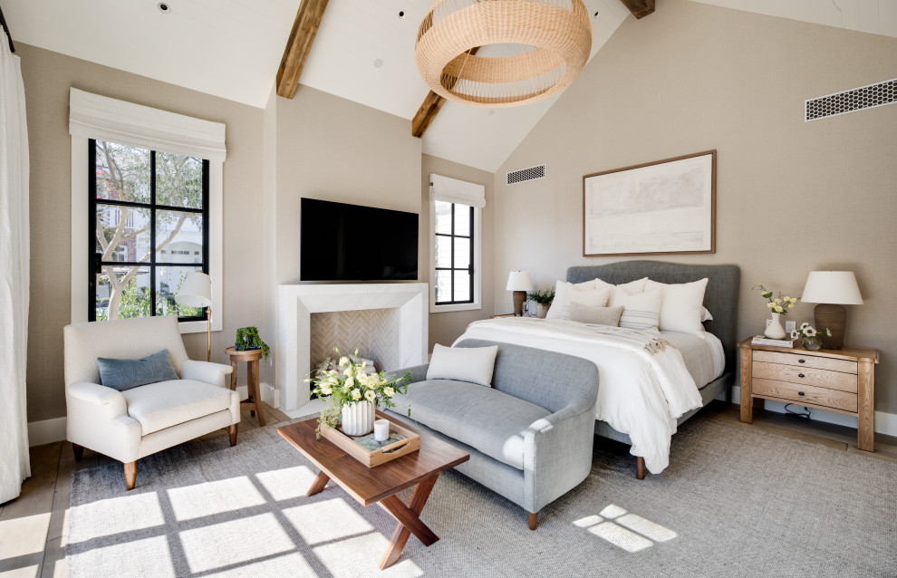 Klassisches Gästezimmer mit beiger Wandfarbe, braunem Holzboden, Kamin, Kaminumrandung aus Stein, braunem Boden, freigelegten Dachbalken und gewölbter Decke in Orange County