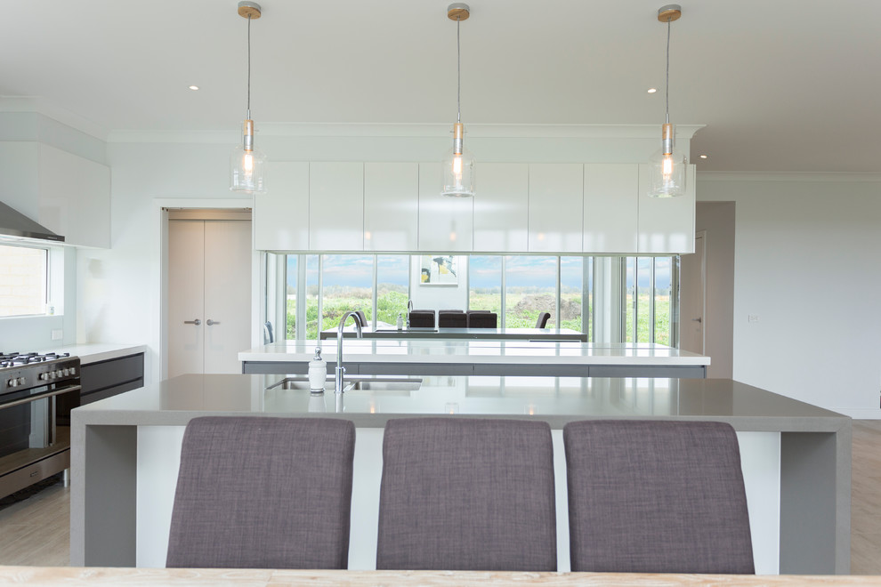 Large modern l-shaped open plan kitchen in Melbourne with a double-bowl sink, flat-panel cabinets, grey cabinets, quartz benchtops, window splashback, stainless steel appliances, travertine floors, with island, grey floor and grey benchtop.