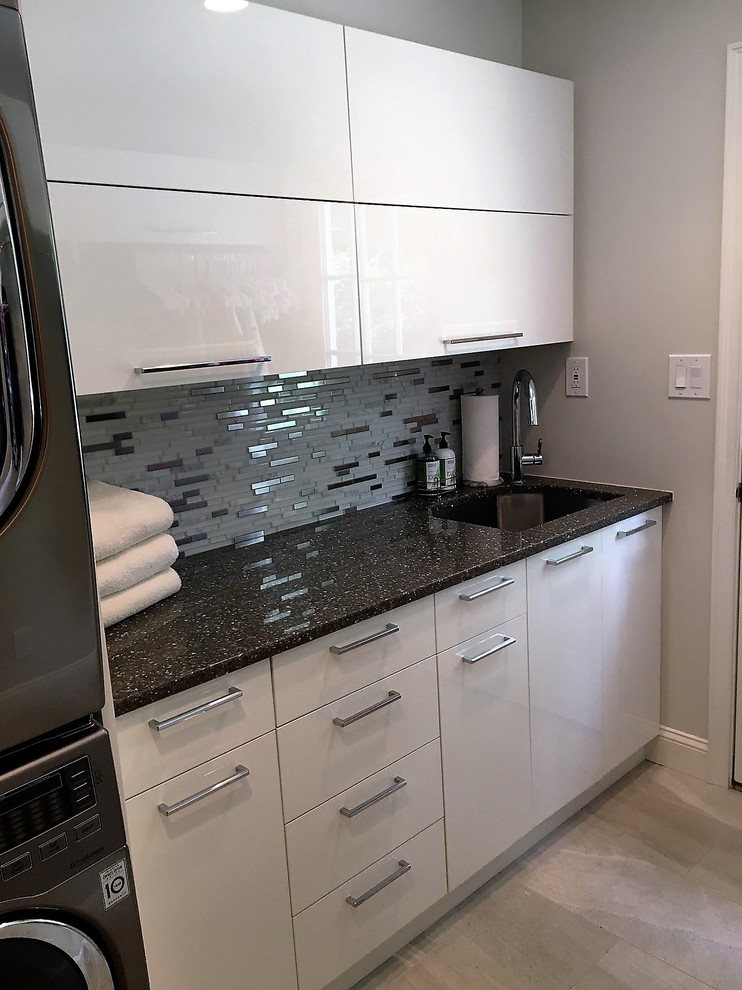 Small transitional single-wall dedicated laundry room in Philadelphia with an undermount sink, flat-panel cabinets, white cabinets, quartz benchtops, grey walls, light hardwood floors, a stacked washer and dryer and black benchtop.