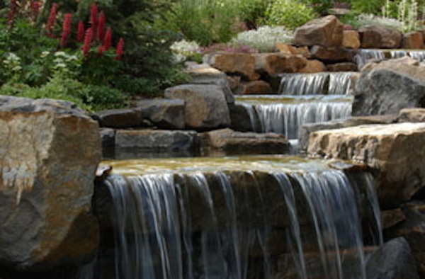 Photo of a huge rustic full sun backyard stone water fountain landscape in Denver.