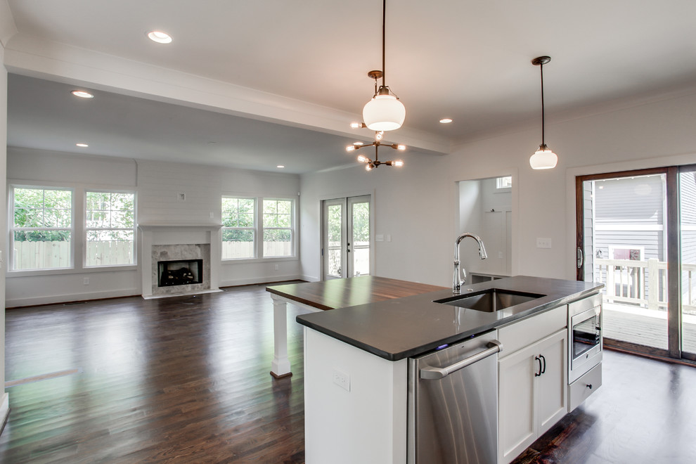 Photo of a mid-sized country galley open plan kitchen in Nashville with an undermount sink, shaker cabinets, white cabinets, quartz benchtops, grey splashback, glass tile splashback, stainless steel appliances, dark hardwood floors and with island.
