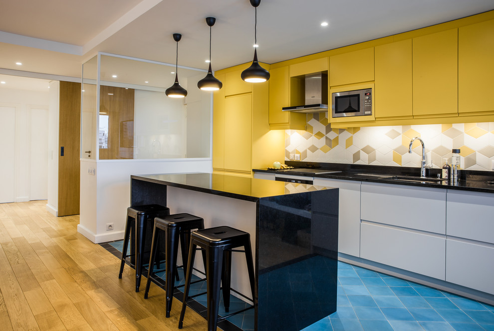 Mid-sized scandinavian single-wall eat-in kitchen in Paris with a double-bowl sink, yellow cabinets, yellow splashback, porcelain splashback, stainless steel appliances, ceramic floors, with island, blue floor and black benchtop.