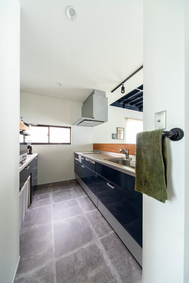 Mid-sized industrial single-wall open plan kitchen in Osaka with an undermount sink, beaded inset cabinets, blue cabinets, stainless steel benchtops, white splashback, with island and grey floor.