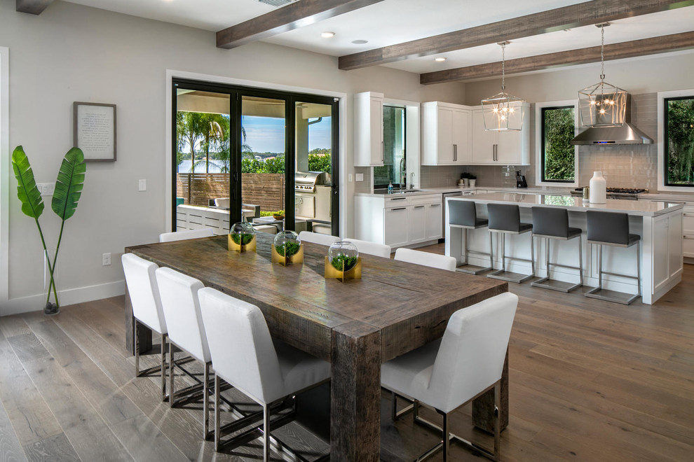 This is an example of an expansive modern u-shaped eat-in kitchen in Tampa with an undermount sink, shaker cabinets, white cabinets, quartz benchtops, grey splashback, glass tile splashback, stainless steel appliances, medium hardwood floors, with island, brown floor and grey benchtop.