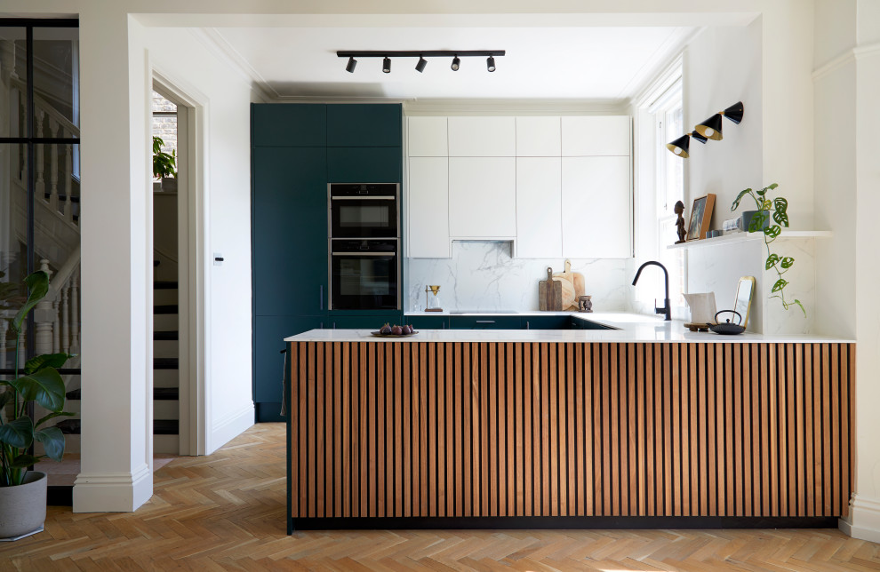 Inspiration for a medium sized modern u-shaped kitchen/diner in London with a built-in sink, flat-panel cabinets, green cabinets, white splashback, black appliances, medium hardwood flooring, an island, white worktops and feature lighting.