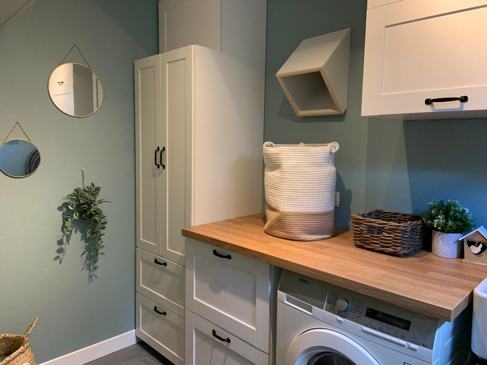 Small single-wall utility room in Other with a single-bowl sink, white cabinets, wood benchtops, white splashback, cement tile splashback, blue walls, ceramic floors, an integrated washer and dryer, grey floor and brown benchtop.