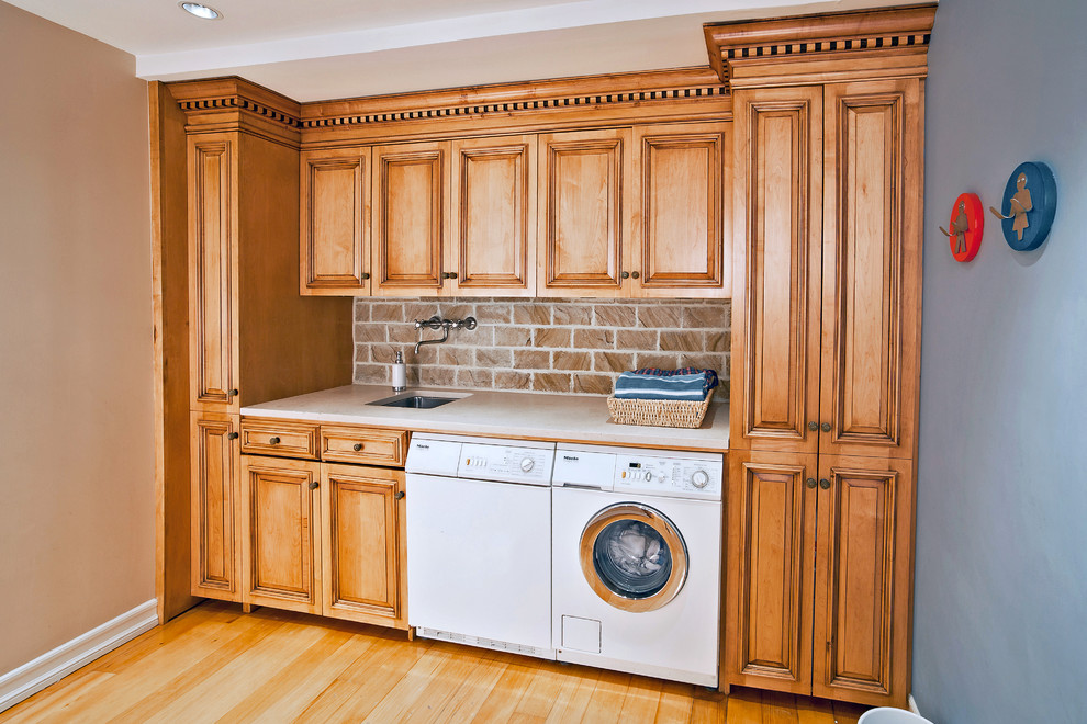 Design ideas for a large traditional single-wall utility room in New York with raised-panel cabinets, granite benchtops, a side-by-side washer and dryer, an undermount sink, medium wood cabinets, blue walls, laminate floors, yellow floor and beige benchtop.