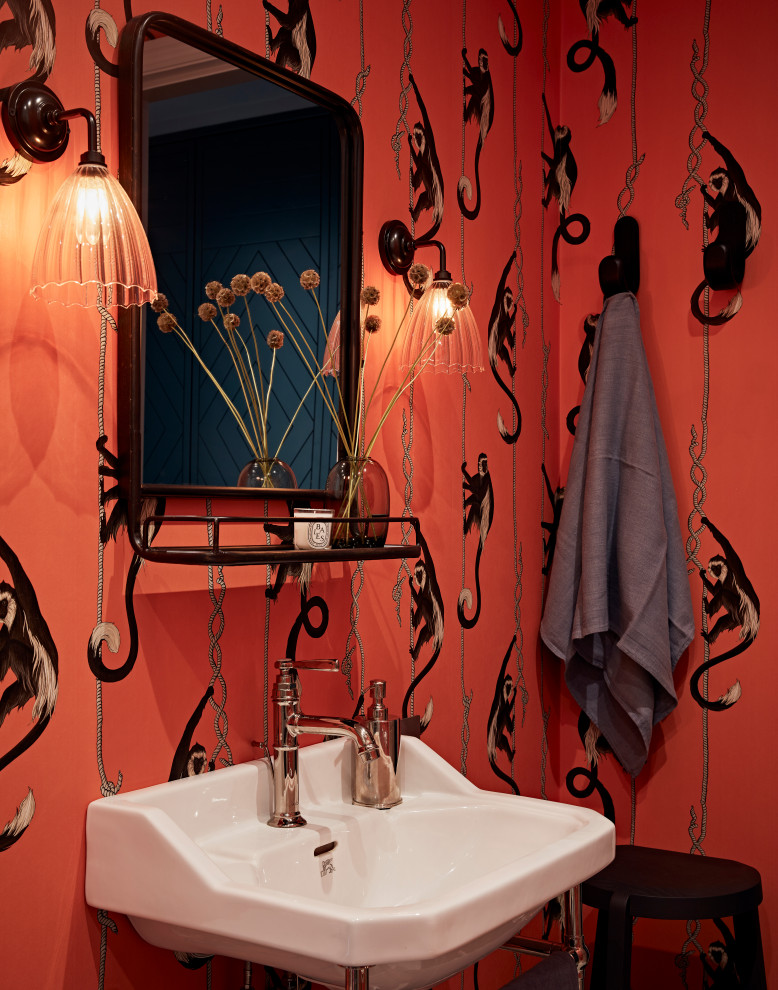 This is an example of a transitional powder room in London with a freestanding vanity, wallpaper, multi-coloured walls, a pedestal sink and white benchtops.