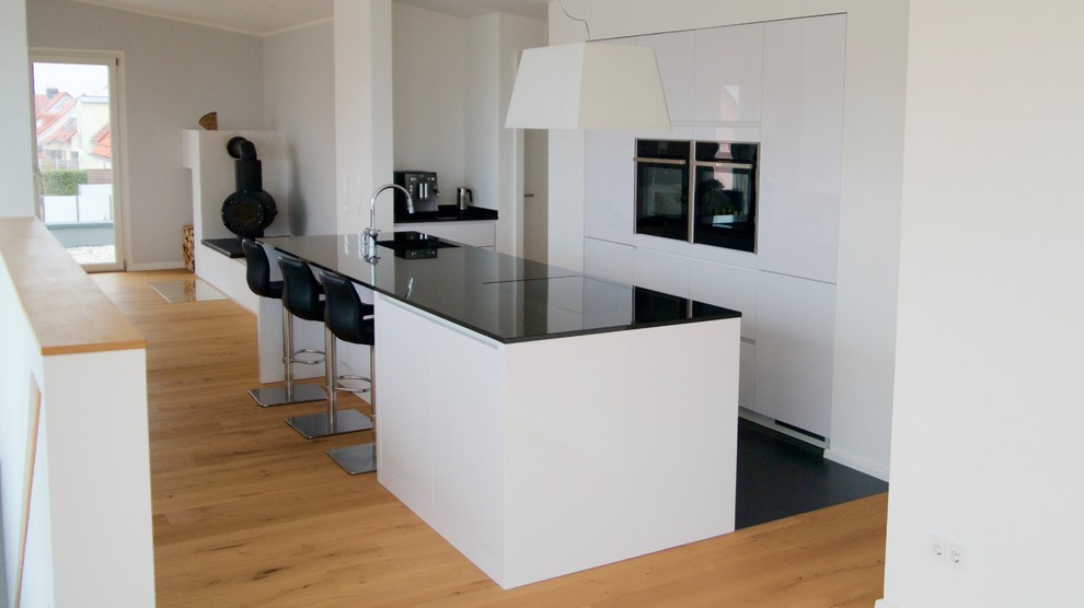 Inspiration for a mid-sized contemporary galley open plan kitchen in Nuremberg with a drop-in sink, flat-panel cabinets, white cabinets, granite benchtops, white splashback, stainless steel appliances, ceramic floors and a peninsula.