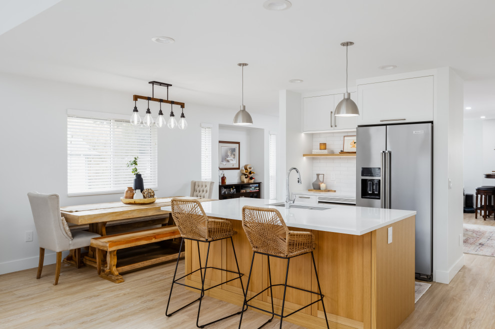 Inspiration for a mid-sized transitional single-wall light wood floor and beige floor eat-in kitchen remodel in Vancouver with an undermount sink, shaker cabinets, white cabinets, quartzite countertops, white backsplash, subway tile backsplash, stainless steel appliances, an island and white countertops