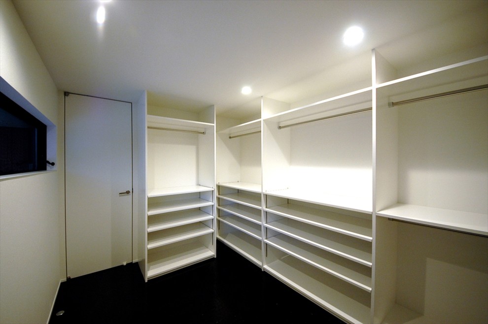 Aménagement d'un grand dressing moderne neutre avec un placard sans porte, des portes de placard blanches et un sol noir.