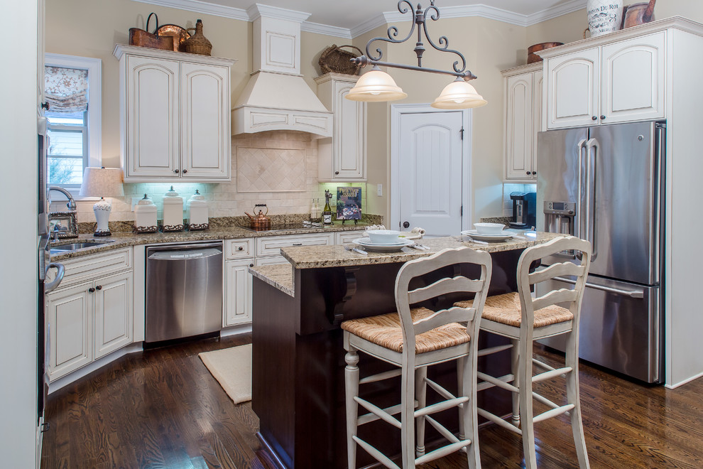 This is an example of a mid-sized transitional u-shaped open plan kitchen in Atlanta with an undermount sink, raised-panel cabinets, white cabinets, granite benchtops, beige splashback, stone tile splashback, stainless steel appliances, dark hardwood floors, with island and brown floor.