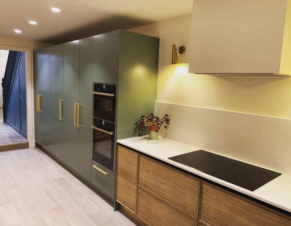 Design ideas for a mid-sized contemporary galley eat-in kitchen in Sussex with a single-bowl sink, flat-panel cabinets, green cabinets, solid surface benchtops, white splashback, stone slab splashback, black appliances, ceramic floors, with island, white floor and white benchtop.