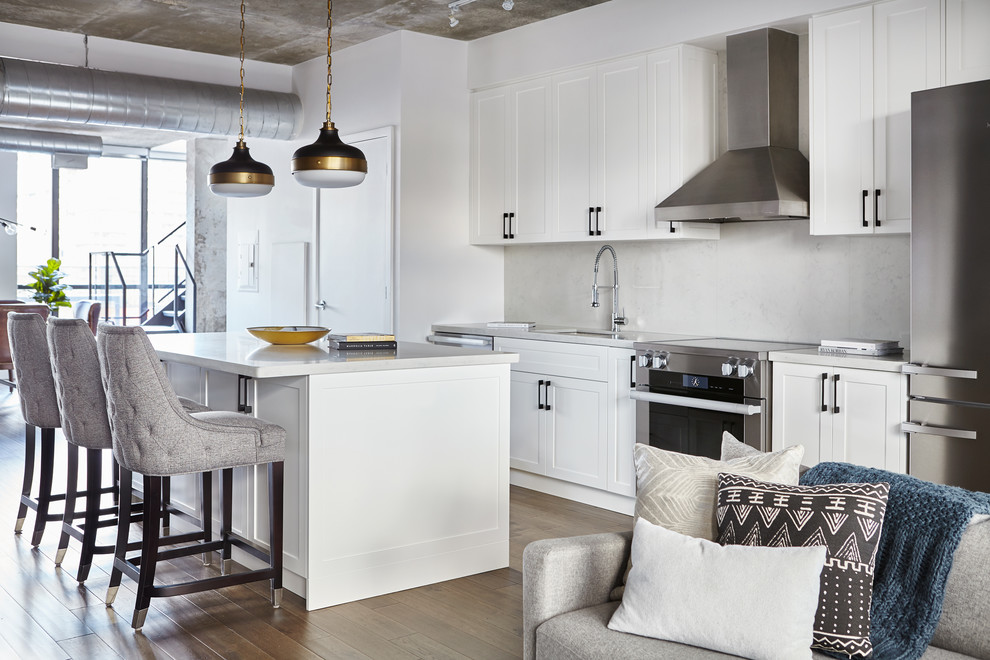 Inspiration for an industrial single-wall open plan kitchen in Toronto with an undermount sink, shaker cabinets, white cabinets, stainless steel appliances, medium hardwood floors, with island, brown floor and beige benchtop.