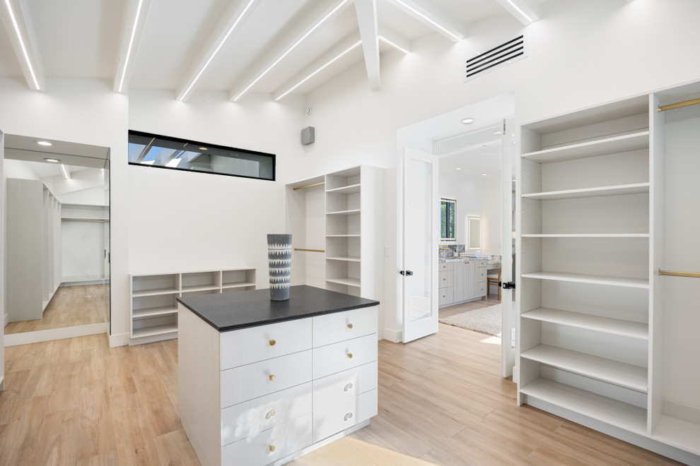 Example of a large transitional gender-neutral porcelain tile, beige floor and exposed beam walk-in closet design with flat-panel cabinets and light wood cabinets