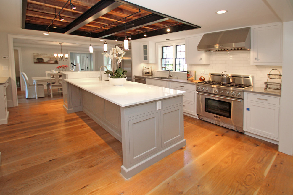 This is an example of a large arts and crafts galley eat-in kitchen in Boston with shaker cabinets, stainless steel cabinets, with island, an undermount sink, solid surface benchtops, white splashback, subway tile splashback, stainless steel appliances, medium hardwood floors and brown floor.