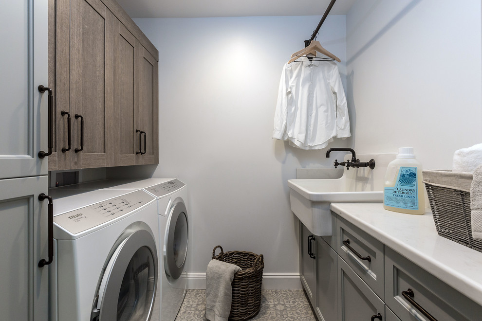 This is an example of a mid-sized utility room in San Francisco with a drop-in sink, glass-front cabinets, medium wood cabinets, quartz benchtops, white walls, ceramic floors, a side-by-side washer and dryer, multi-coloured floor and white benchtop.