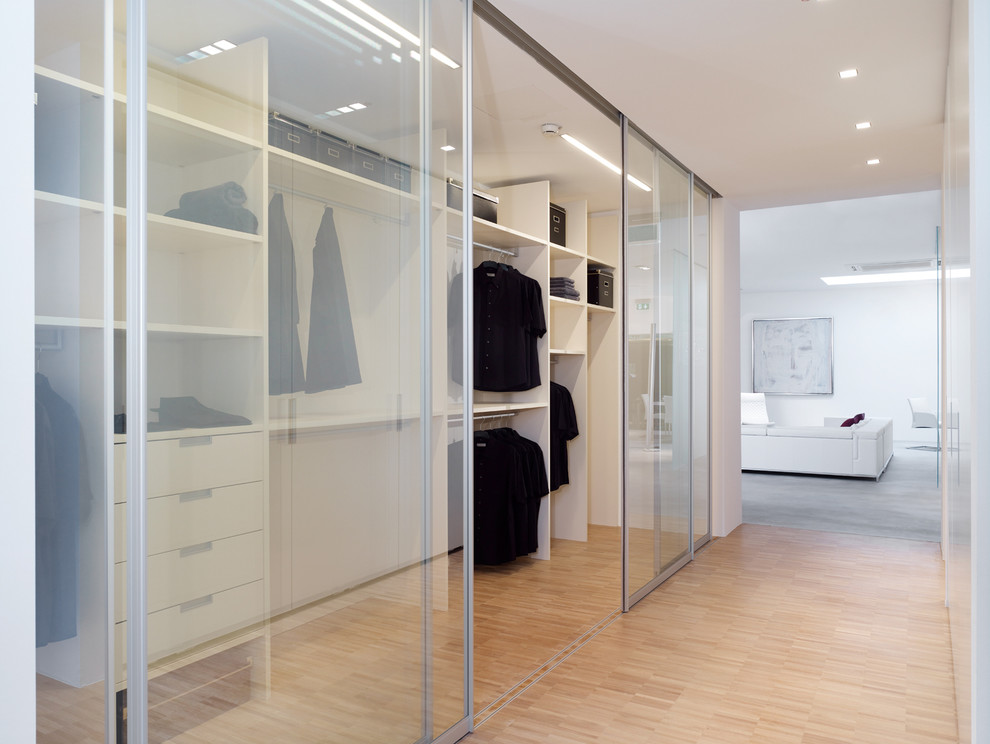 Large contemporary gender-neutral walk-in wardrobe in Dusseldorf with open cabinets, white cabinets and bamboo floors.