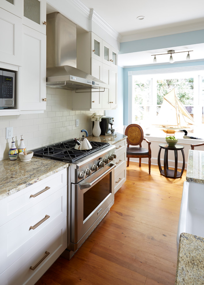 Transitional medium tone wood floor eat-in kitchen photo in DC Metro with a farmhouse sink, recessed-panel cabinets, white cabinets, granite countertops, white backsplash, subway tile backsplash, stainless steel appliances and an island
