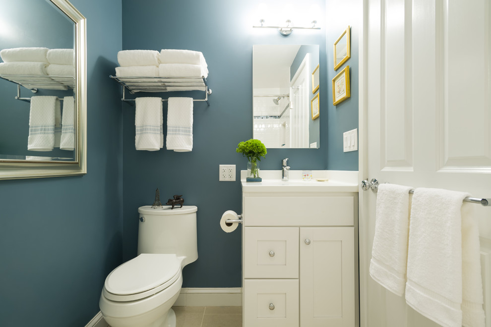 This is an example of a small transitional 3/4 bathroom in Boston with white cabinets, a one-piece toilet, white tile, shaker cabinets, an alcove tub, a shower/bathtub combo, porcelain tile, blue walls, travertine floors, an undermount sink and solid surface benchtops.