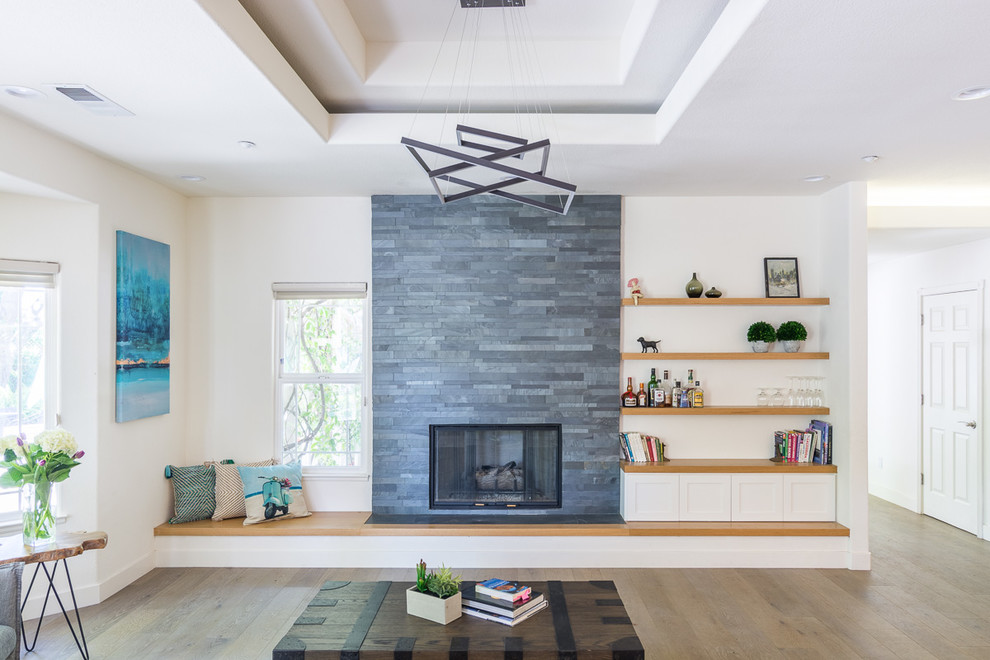 Photo of a large transitional open concept living room in San Francisco with a library, white walls, medium hardwood floors, a standard fireplace, a tile fireplace surround, no tv and multi-coloured floor.