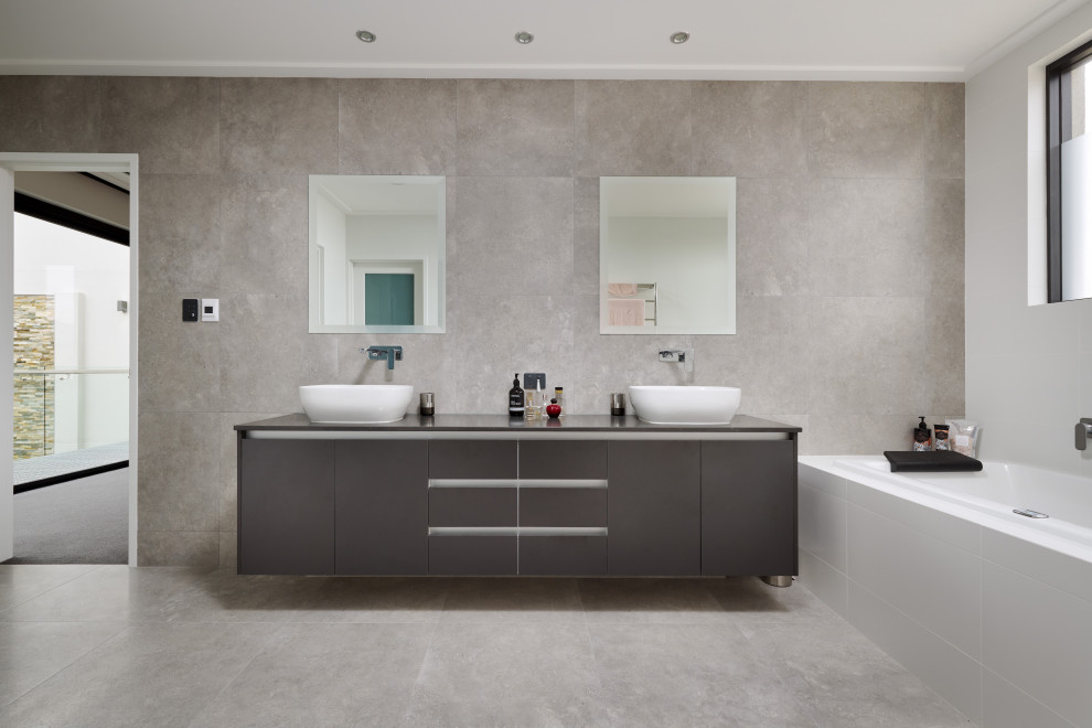 Modern inredning av ett stort grå grått en-suite badrum, med luckor med profilerade fronter, grå skåp, ett platsbyggt badkar, en öppen dusch, en toalettstol med hel cisternkåpa, grå kakel, porslinskakel, grå väggar, klinkergolv i porslin, ett konsol handfat, granitbänkskiva, grått golv och med dusch som är öppen