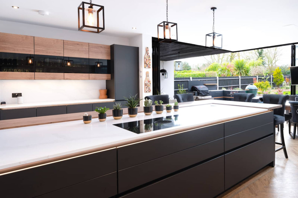 Open concept kitchen - large industrial u-shaped light wood floor and brown floor open concept kitchen idea in Hertfordshire with an integrated sink, flat-panel cabinets, black cabinets, quartzite countertops, white backsplash, black appliances, an island and white countertops