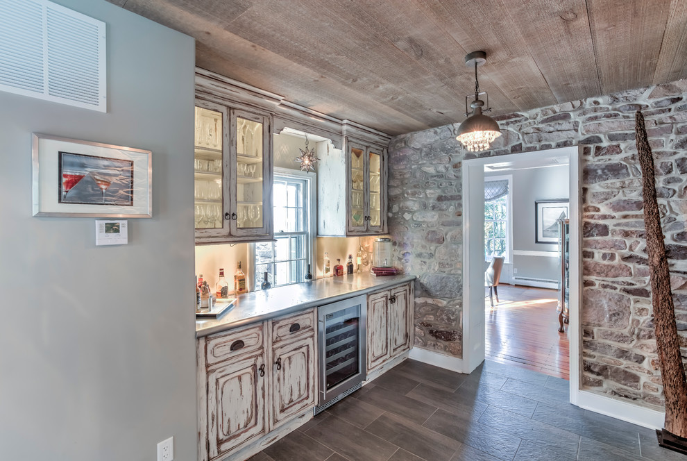 Photo of a mid-sized contemporary single-wall wet bar in Philadelphia with glass-front cabinets, distressed cabinets, stainless steel benchtops, beige splashback and slate floors.