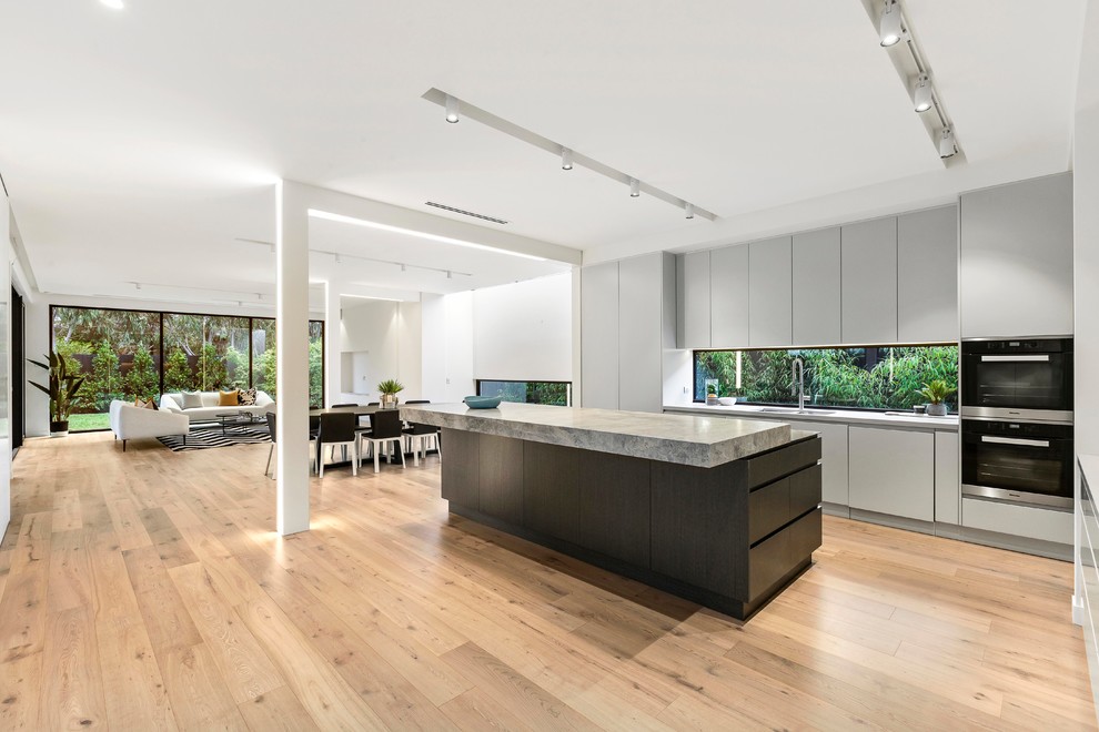 Mid-sized contemporary single-wall kitchen pantry in Melbourne with an undermount sink, grey cabinets, limestone benchtops, grey splashback, glass sheet splashback, stainless steel appliances, medium hardwood floors, with island and grey benchtop.
